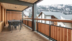 Un terrazzo in legno con tavolo e sedie, una ringhiera di legno e vista su montagne innevate.