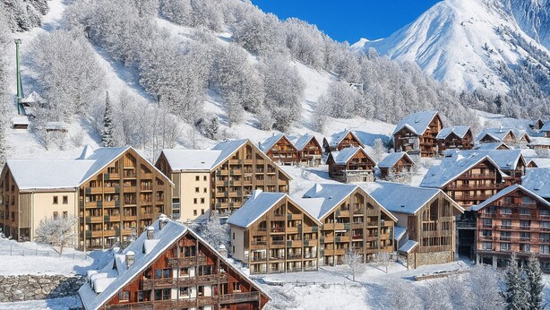 Una località montana innevata con chalet in legno e una seggiovia.