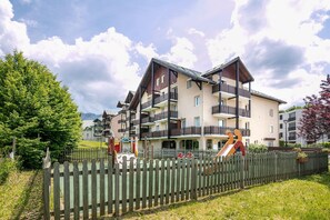 Un immeuble à plusieurs étages doté de balcons, d’une aire de jeux et d’une clôture en bois.