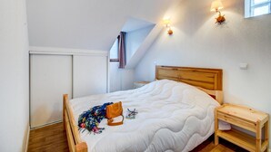 Une chambre à coucher avec un lit en bois, une table de chevet, une lampe fixée au mur et une fenêtre.