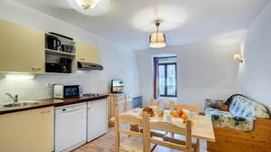 Une cuisine compacte équipée d’un four à micro-ondes, d’une machine à café et d’un lave-vaisselle. On y trouve une table à manger avec des chaises, ainsi qu’un canapé dans l’espace salon.