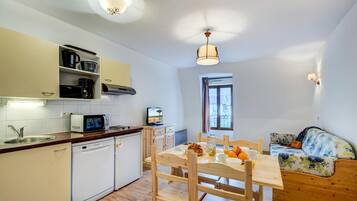 Cocina compacta equipada con microondas, cafetera y lavavajillas. Cuenta con una mesa de comedor con sillas y un sofá en la sala.