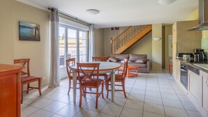 Uma sala de jantar com uma mesa redonda e cadeiras, um sofá, uma cozinha com fogão e uma escada.