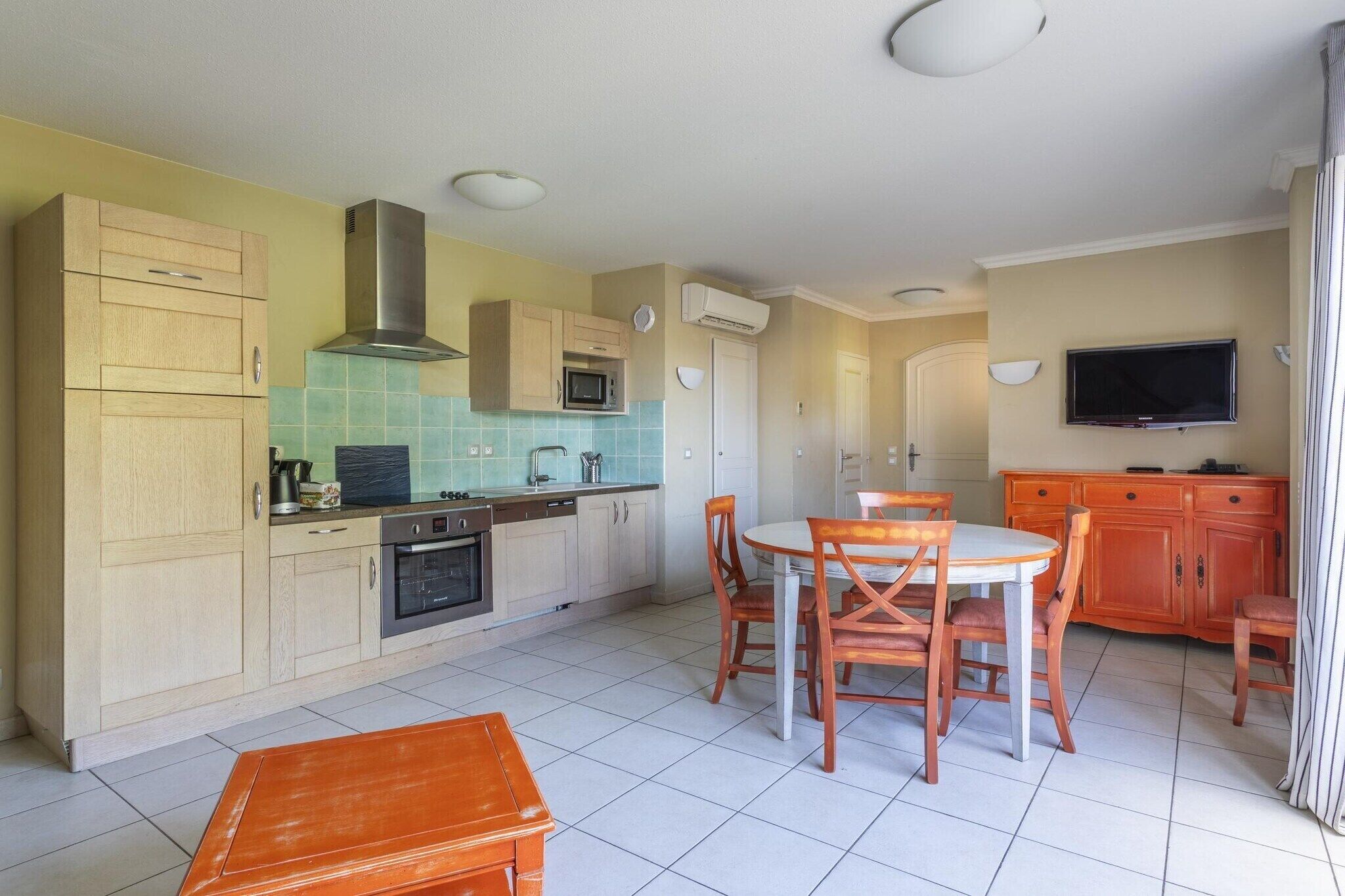 Una cocina compacta con microondas, estufa y pileta, una mesa de comedor con sillas, y un televisor colocado en la pared.