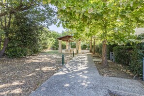 Un sendero que conduce a una zona con asientos techada, rodeada de árboles y follaje.