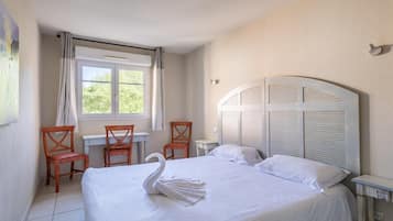 Een hotelkamer met een bed, een bureau, twee stoelen, een raam met gordijnen en een wandlamp.