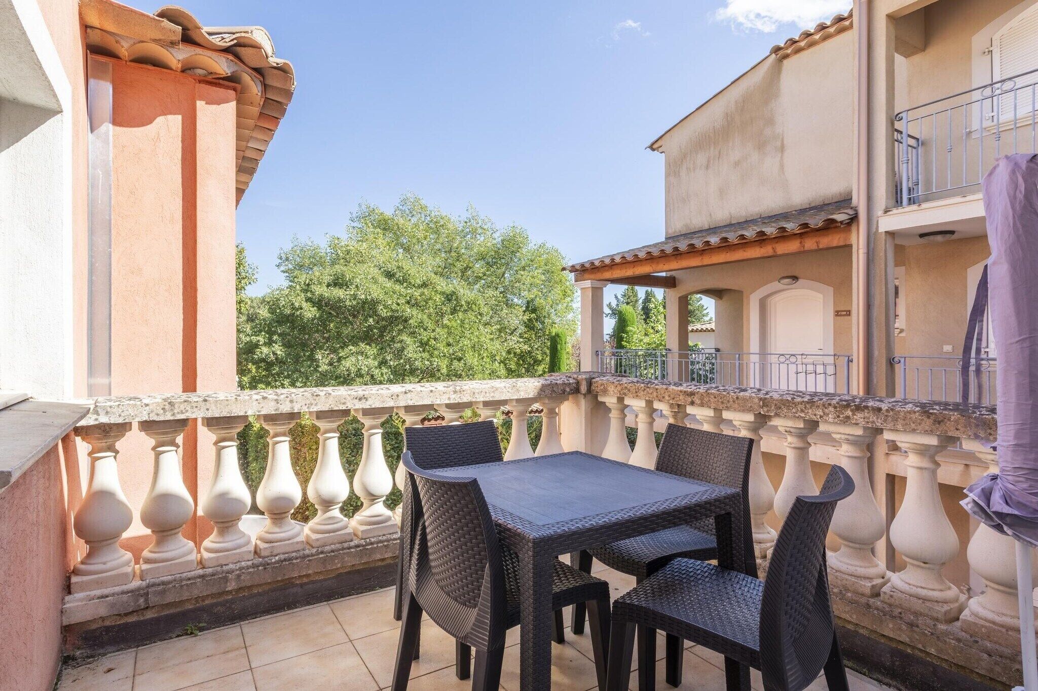 A balcony with a table and chairs, a railing, and a building in the background.
