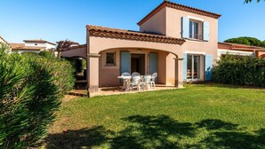 Una casa a due piani con un patio, un piccolo giardino e un cielo azzurro intenso.