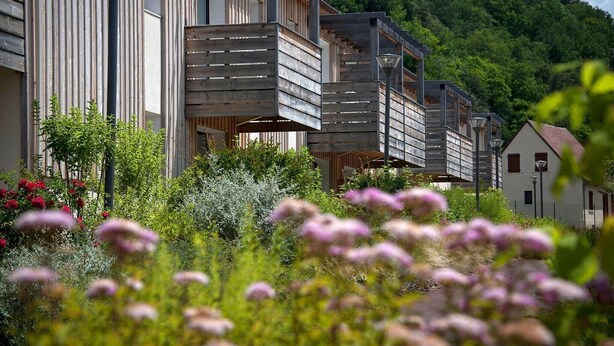 Edifici modern amb lamel·les de fusta, envoltat de vegetació i flors exuberants.
