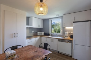 Una cocina moderna con armarios blancos, una mesa de comedor de madera y una lámpara colgante.