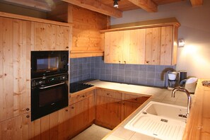 Eine Küche mit Holzschränken, einem Einbauofen, einer Mikrowelle, einem Spülbecken und einer Kaffeemaschine.