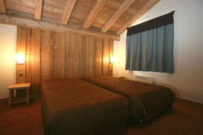 Ein Zimmer mit zwei Betten, Holzwänden, einem kleinen Tisch und zwei Wandleuchten.