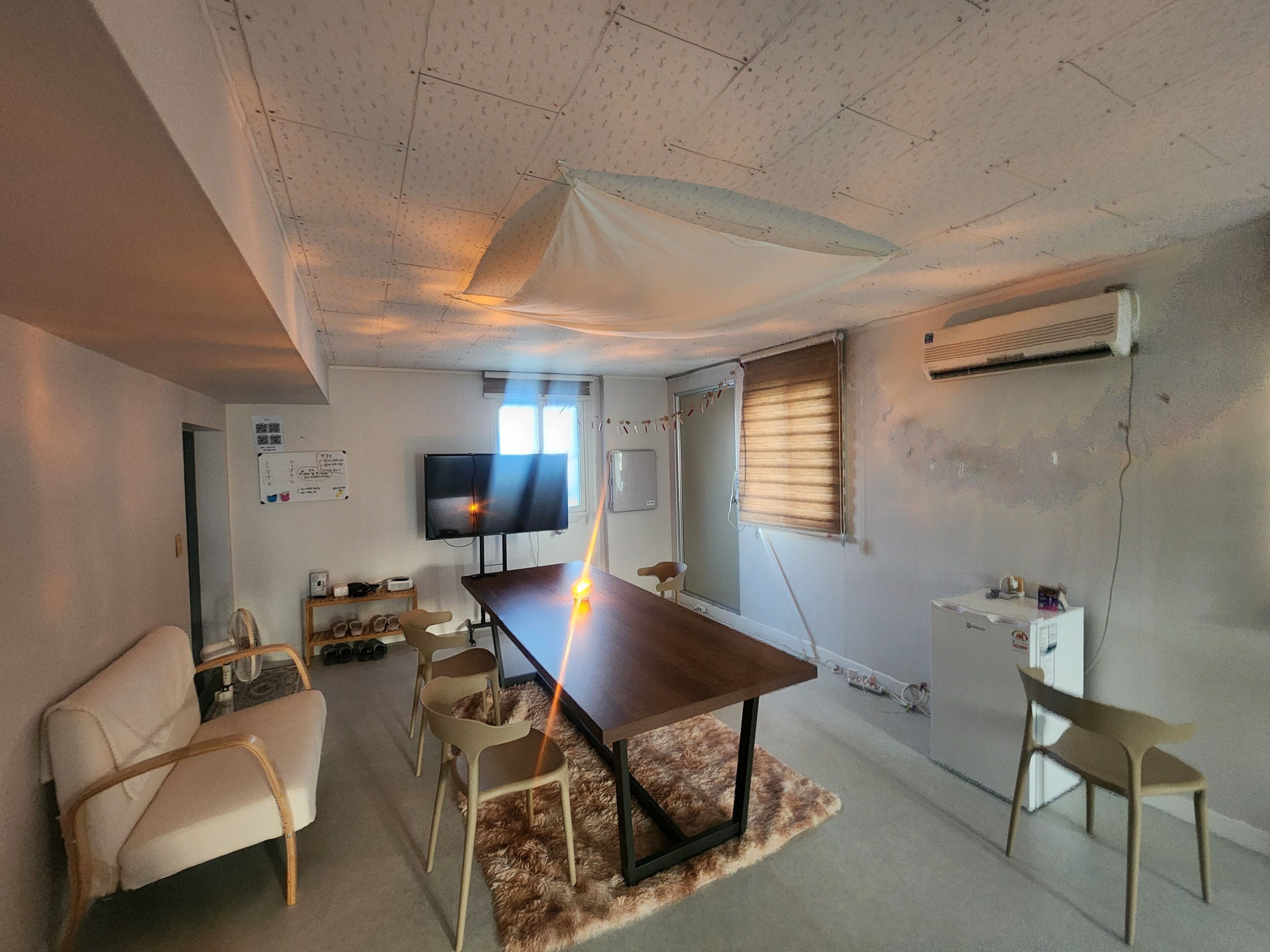 A room with a large table, chairs, a television, and a window with blinds.