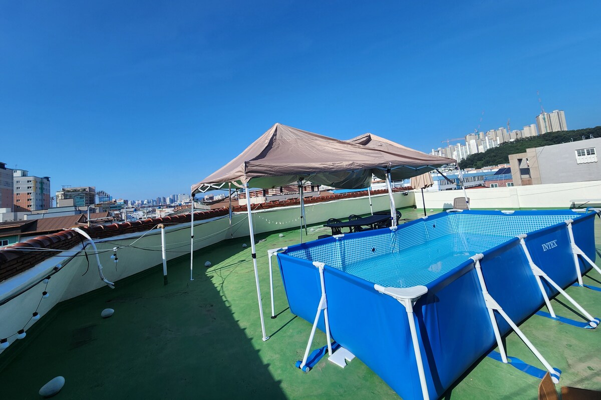 A rooftop pool area with a blue pool, a covered seating area, and boats.