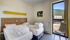 Ett hotellrum med två sängar, en stol, ett fönster med utsikt över en byggnad och ett gult konstverk på väggen.