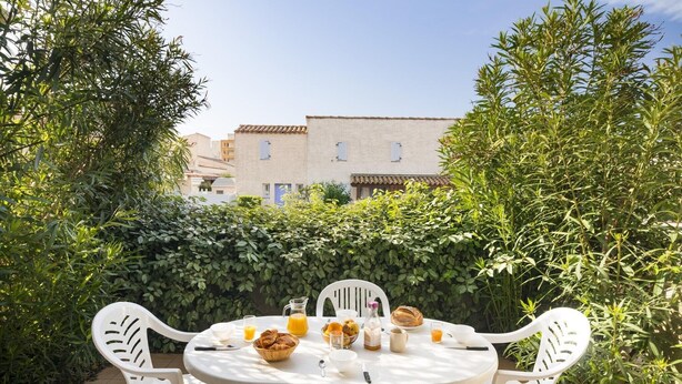 Un tavolo rotondo con sedie bianche, un cesto di croissant, una caraffa di succo d'arancia e una bottiglia di latte.