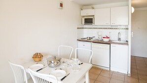 Un tavolo da pranzo con sedie bianche, una cucina con mobili bianchi, un forno a microonde e un lavandino.