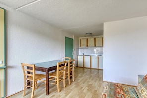 A compact kitchen with a dining table and chairs, a green door, and a patterned rug.