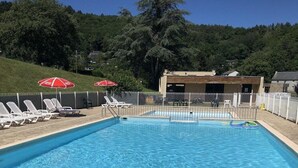 Et rektangulært swimmingpool med krystalklart, blå vand, omgivet af et hvidt hegn og med parasoller.
