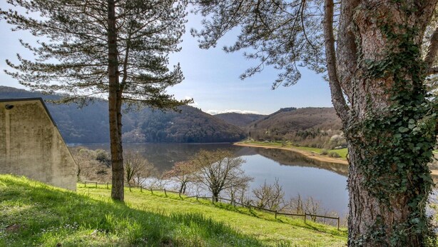 Une vue paisible sur un lac, avec une structure en béton, des arbres et une zone herbeuse.