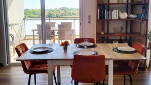 Een eetgedeelte met een tafel gedekt voor twee personen, een boekenkast en uitzicht op groen via een schuifdeur.