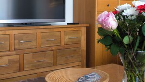 A wooden cabinet with a television on top, a wooden table with a placemat, and a vase with flowers. - Cozy vacation apartment in Winsen an der Luhe for 2-3 persons (Winsen (Luhe))