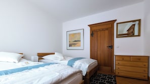 Une chambre avec deux lits, une armoire en bois, une commode et un tableau accroché au mur.