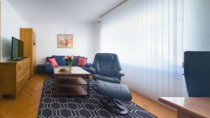 Un salon moderne comprenant un canapé, un fauteuil massant, une table basse et un téléviseur posé sur un meuble en bois.