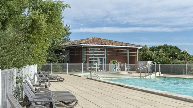 Zona de piscina con sillones de descanso, un edificio con techo de tejas y piscina cercada.