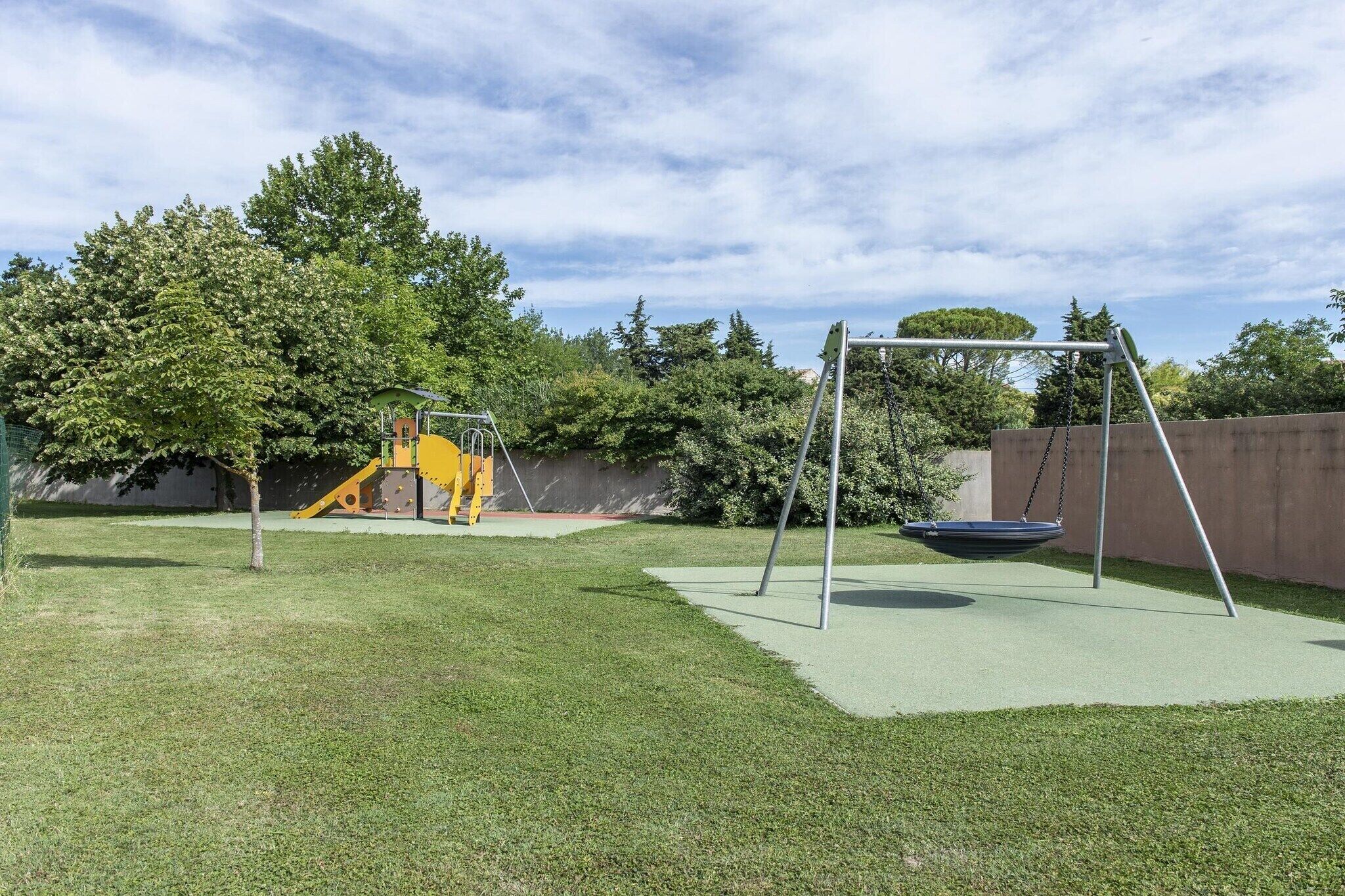 A playground with a swing set and a slide, surrounded by grass and trees.