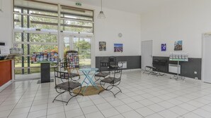 Un espacio interior amplio con un ventanal grande, una mesa con sillas, un tablón de anuncios y una máquina expendedora.