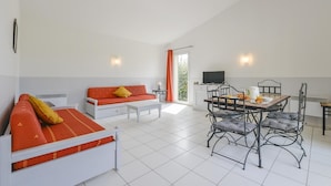 Um quarto com sofá, mesa de jantar com cadeiras, televisão e janela com cortinas.