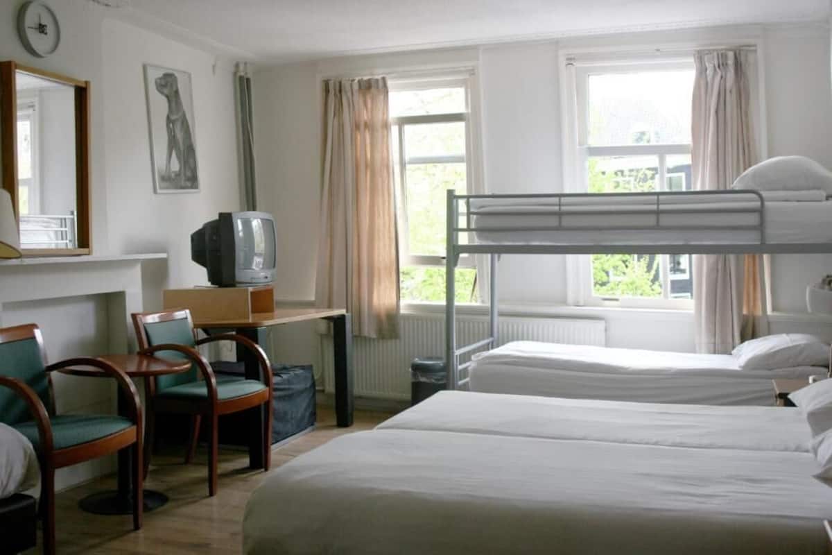 A room with bunk beds, a desk with a television, chairs, and a window with curtains.