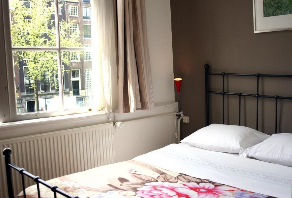 Un lit avec du linge de lit blanc, une fenêtre avec des rideaux et un radiateur.