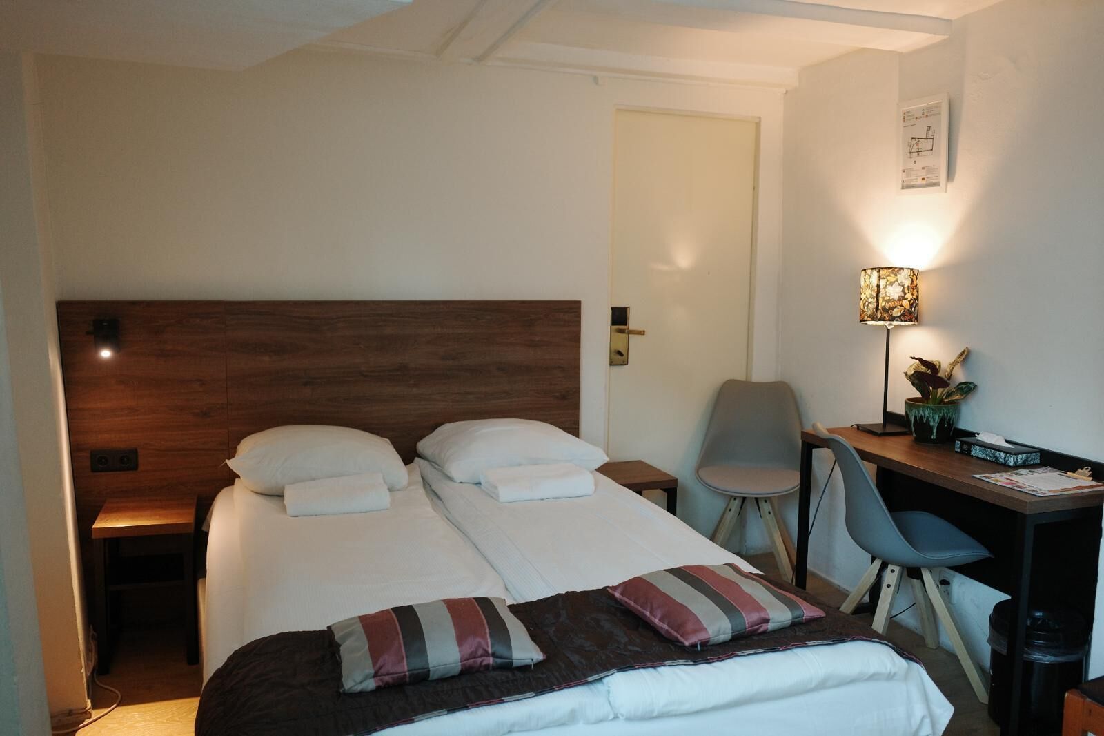 A hotel room with a double bed, a desk, a chair, and a lamp.