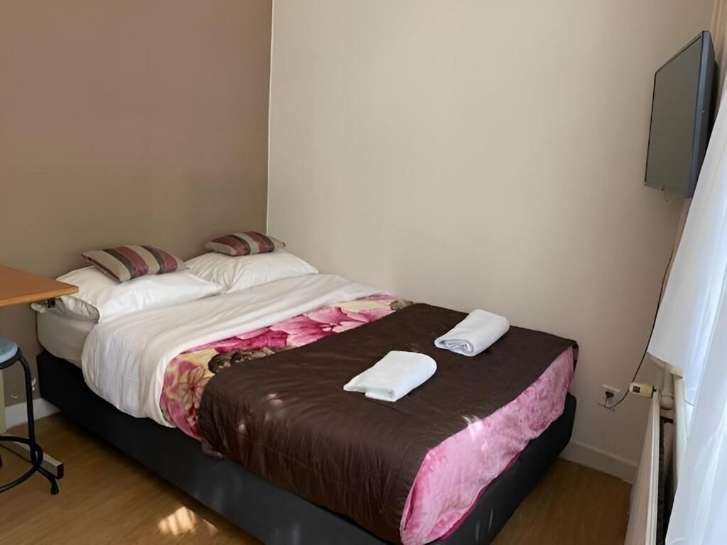 Een slaapkamer met een bed, kussens, een bureau en een flatscreen televisie.