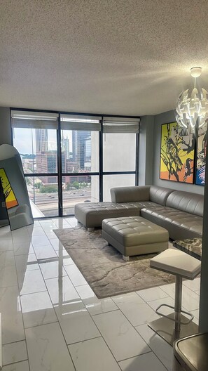 A modern living room with a large window, a sofa, a coffee table, and a floor lamp. - Luxury High-Rise Condo w/ City Views Marta Bus & Train Access Free Parking (Atlanta)
