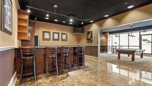 Uma área de bar com mesa de bilhar, banquetas e quadros nas paredes.