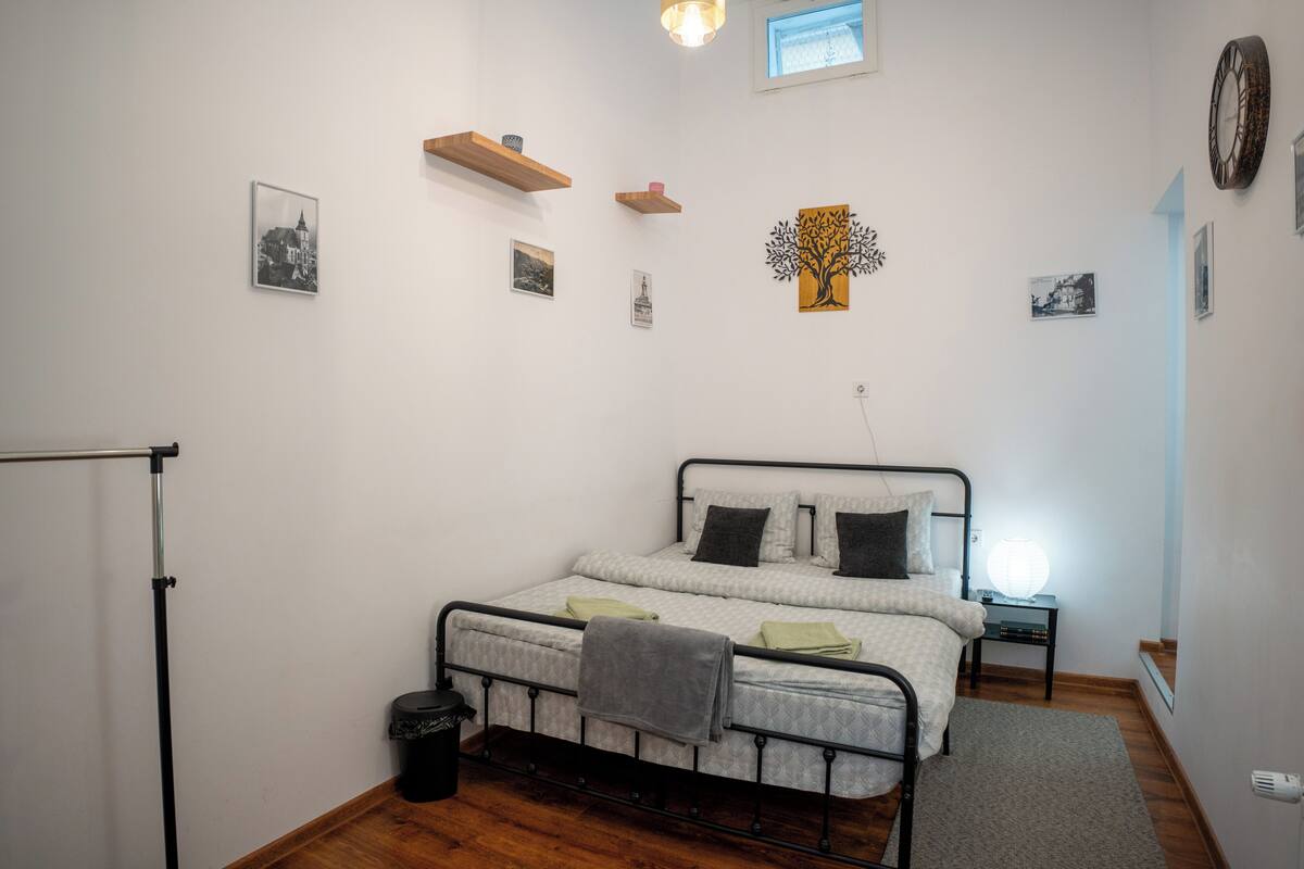 Un dormitorio con cama, una mesita de noche, un reloj en la pared y una ventana.