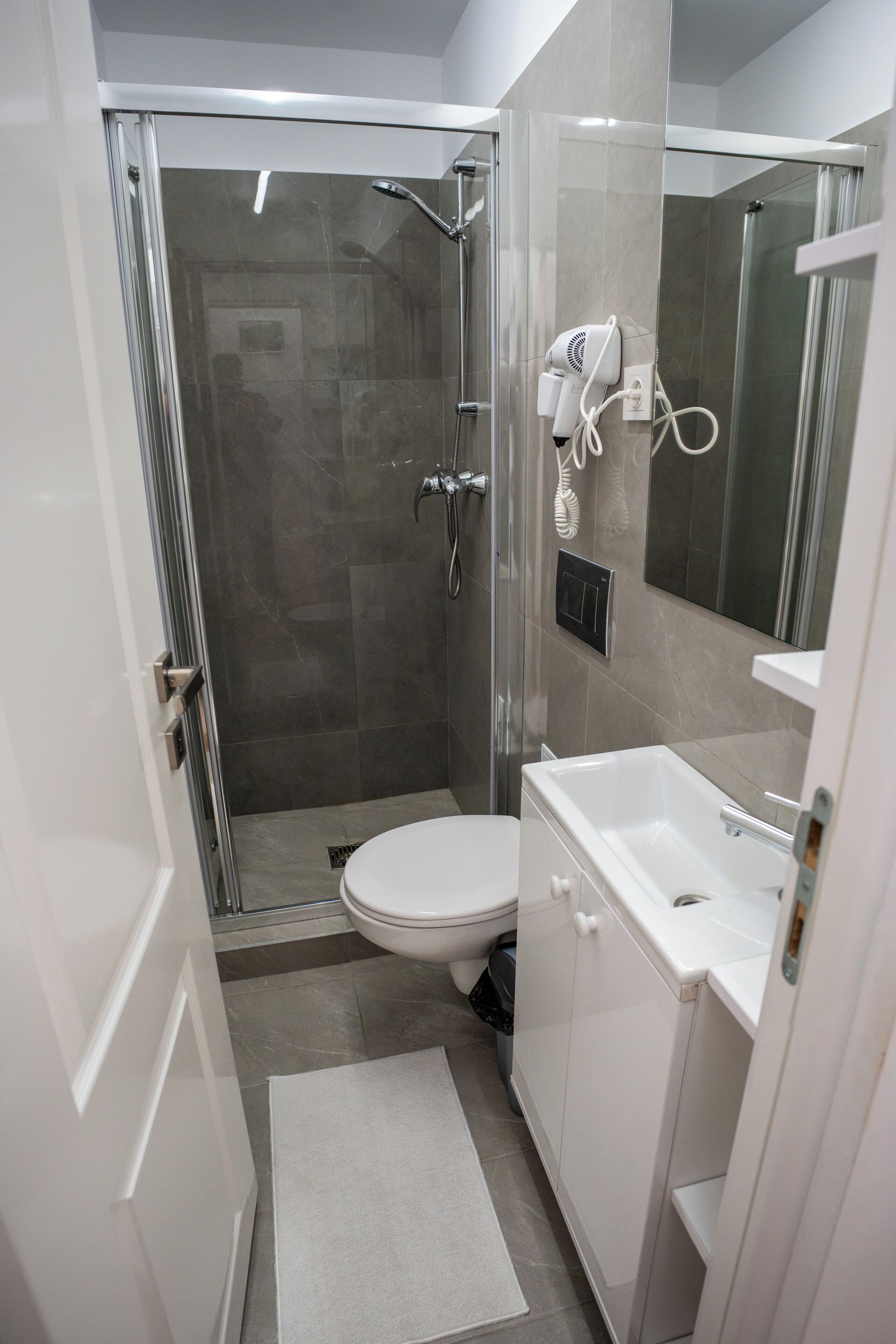 Een moderne badkamer met een glazen douchecabine, een wit toilet en een wastafel met spiegel.