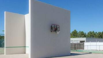 Een basketbalveld met een ring, een witte muur en een heldere lucht.