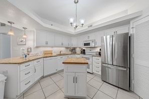 A modern kitchen with white cabinets, stainless steel appliances, and a wooden island. - Summer House 503B (Orange Beach)