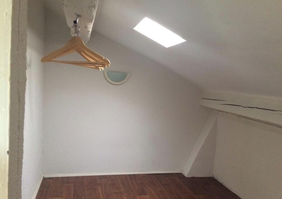 Et rum med skrå vægge, en træbøjle og en lille vægmonteret lampe.