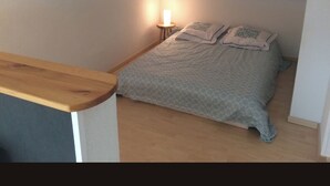 Et soveværelse med seng, et natbord, en lampe og synlige træbjælker.
