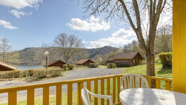 A lakeside view with wooden cabins, a yellow railing, and a table with chairs.