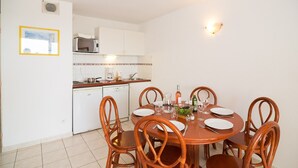 Uma sala de jantar com uma mesa de madeira redonda, seis cadeiras e uma cozinha ao fundo.