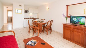 Quarto com mesa de jantar, cadeiras, televisão, armário de madeira e uma cadeira vermelha.