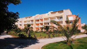 Um hotel com vários andares e varandas, rodeado por jardins bem cuidados e palmeiras.