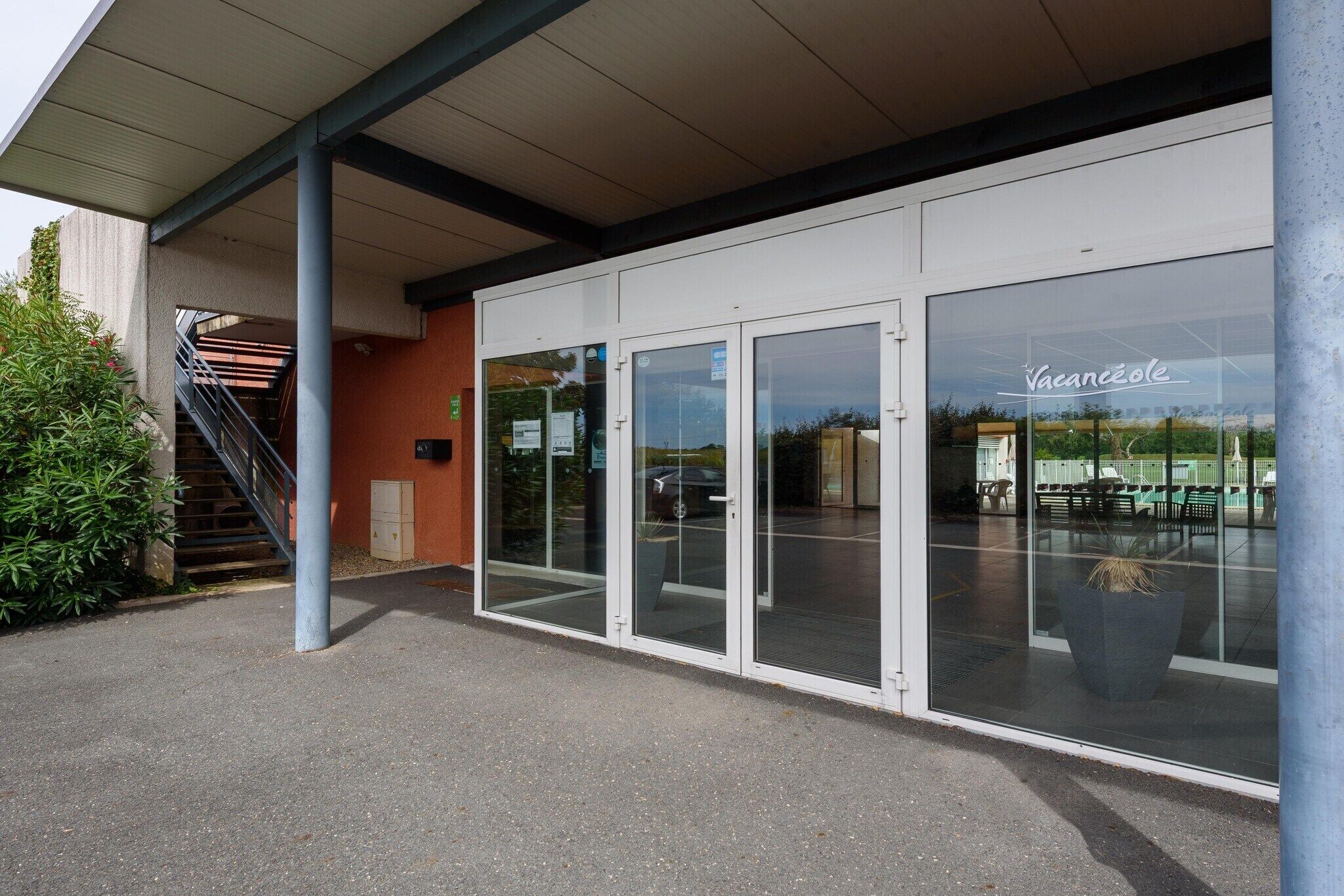 Un bâtiment doté d’une entrée abritée, de portes vitrées et d’un espace extérieur aménagé avec des sièges, visible de l’extérieur.