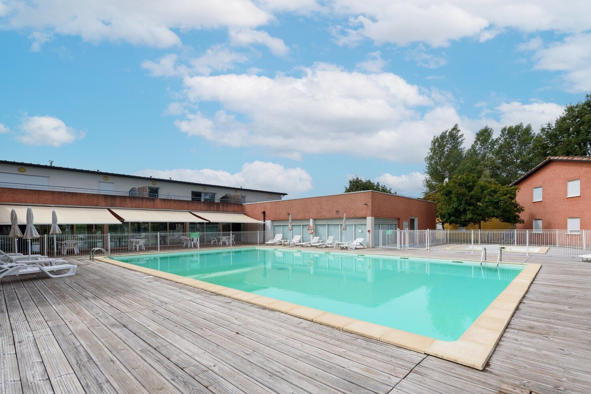 Une piscine avec des chaises longues, une terrasse en bois et un bâtiment à la façade en briques.